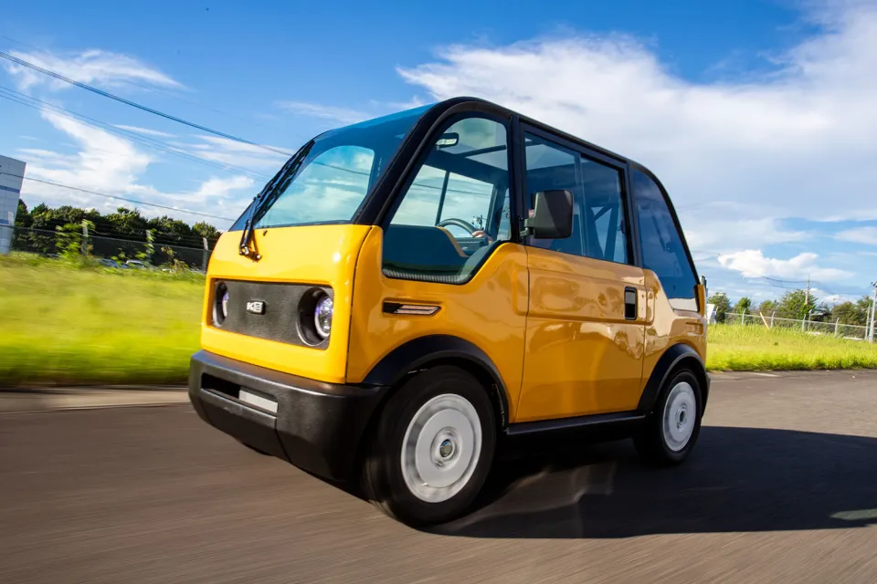 Yellow single-seat Japanese electric vehicle drivign down road.